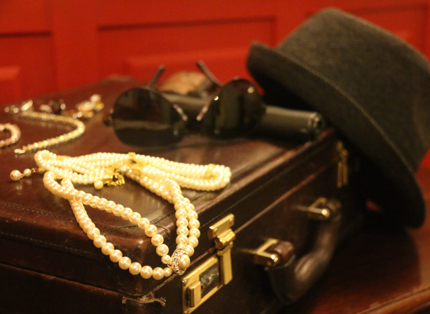 Image of jewels, sunglasses, and a hat on top of a briefcase