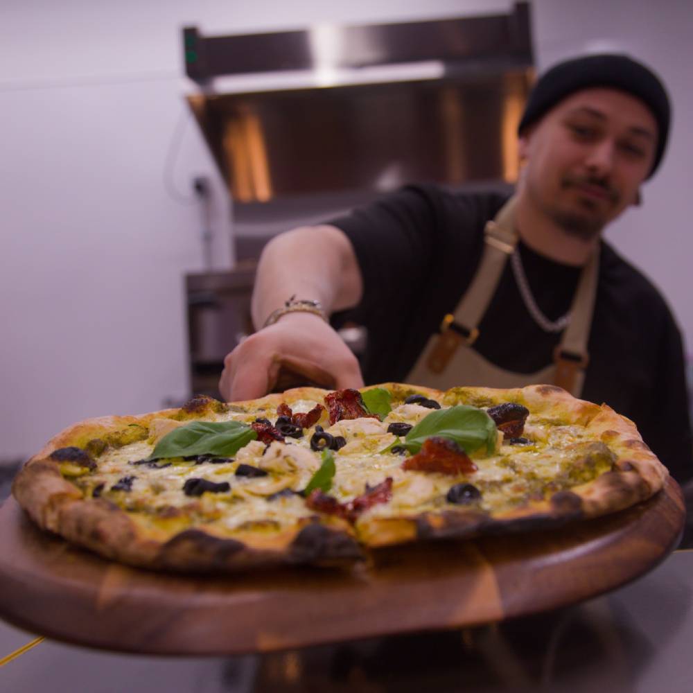 Pizza Held Out on Board by Chef The Comet Club